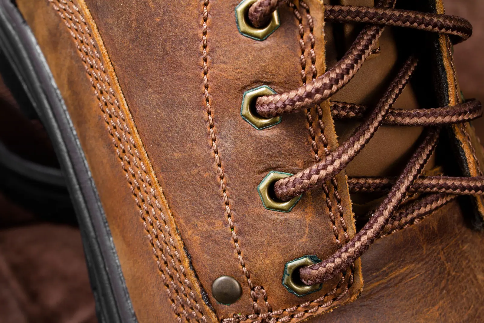 Close detail of a laced brown leather boot with brass eyelets.
