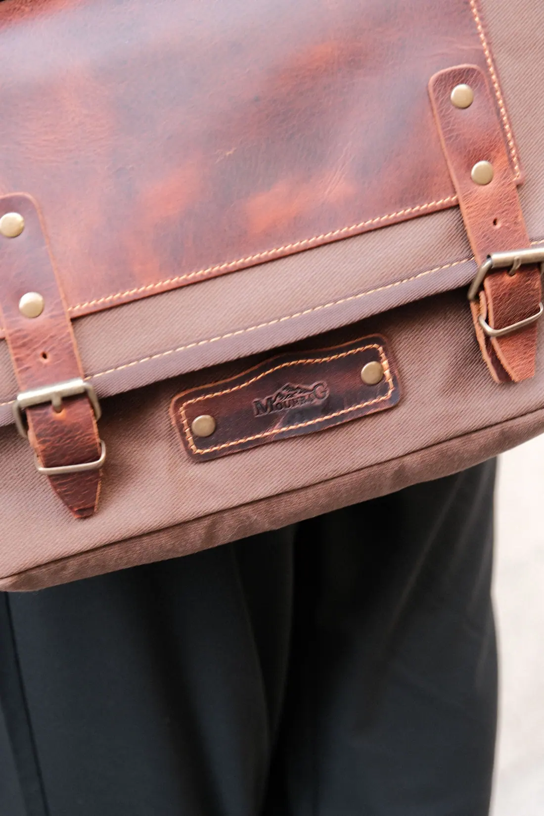 A tan leather messenger bag with brass buckles carried at hip height.